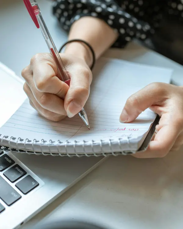 Main en train d’écrire dans un carnet à côté d’un ordinateur portable